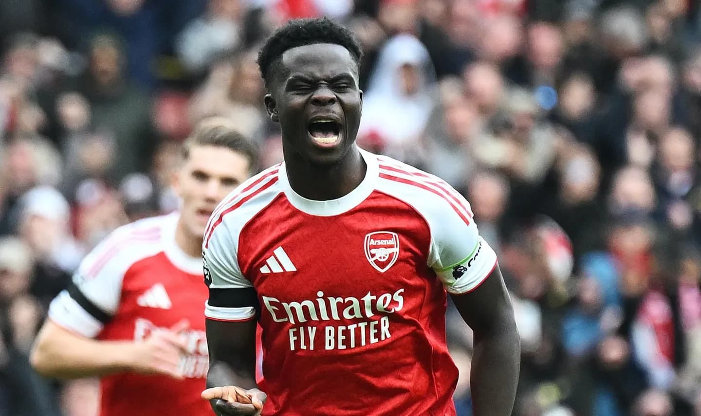 Bukayo Saka wearing the Arsenal red and white home kit, dribbling past a defender — England winger and FPL midfielder rated high fatigue risk for GW1 2026/27